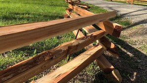 Una valla de madera rústica que lleva a una cabaña con techo rojo, rodeada de césped y árboles.