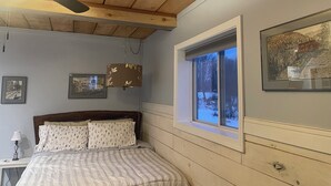 Un dormitorio con cama, ventilador de techo, ventana con vistas y dos cuadros en la pared.