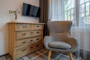 Ein Zimmer mit einem Holzkleiderschrank, einem Fernseher, einem Sessel und einem Fenster mit Vorhängen.