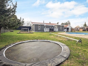 Un patio trasero residencial con un trampolín, una piscina, una casa con porche y un cobertizo.