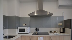 Cozinha moderna com coifa de aço inoxidável, micro-ondas, cafeteira e chaleira sobre a bancada.