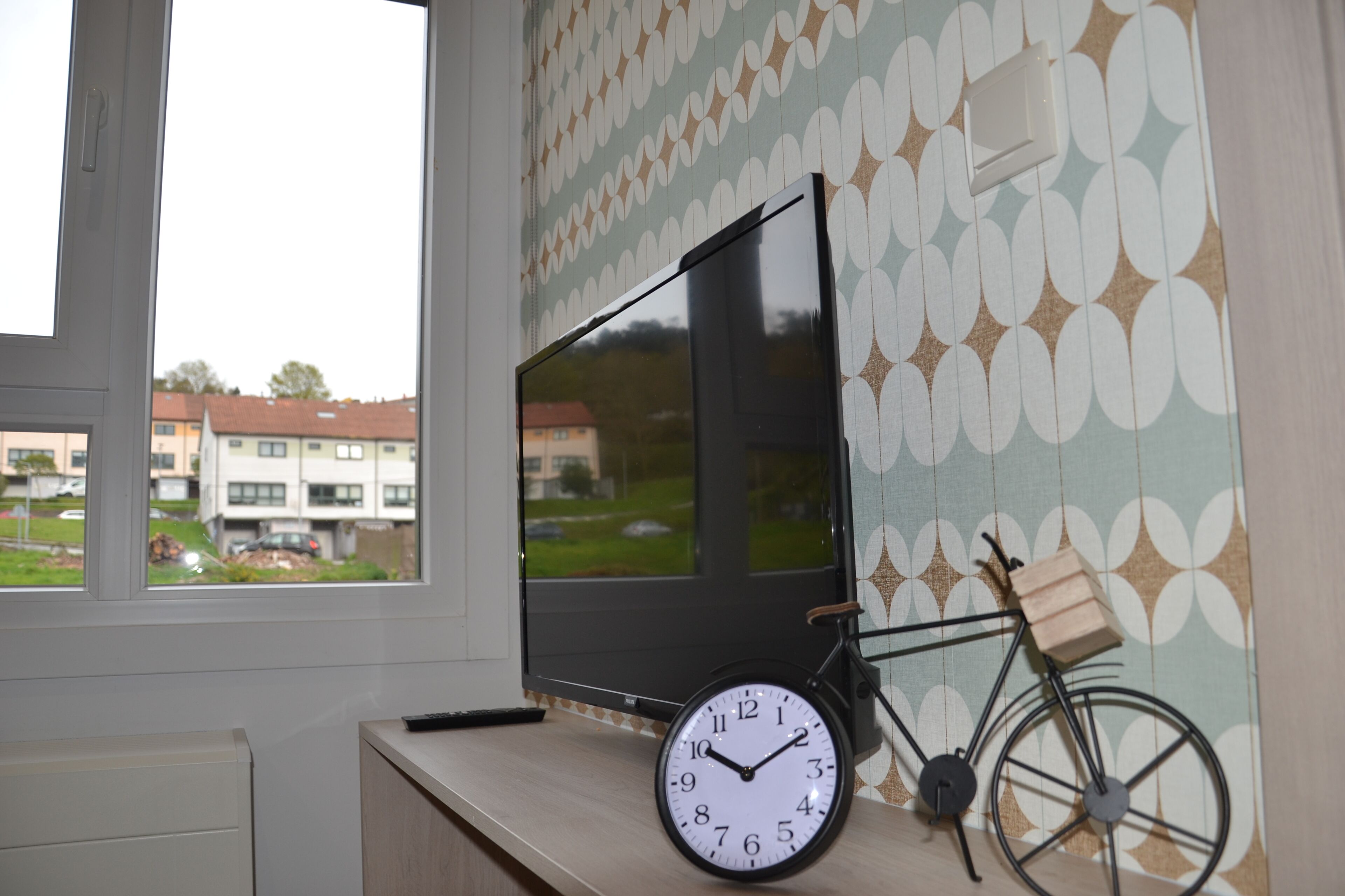 Una habitación con un ventanal grande, un televisor de pantalla plana, una bicicleta y un reloj de pared.
