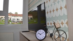 Quarto com uma janela grande, televisão de tela plana, bicicleta e relógio de parede.