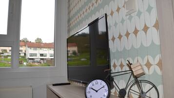 Una habitación con un ventanal grande, un televisor de pantalla plana, una bicicleta y un reloj de pared.