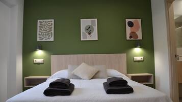 Una cama bien hecha con dos toallas dobladas, un cabecero de madera y tres lámparas fijadas a la pared.