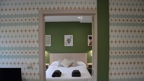 Quarto de hotel com cama, almofadas, mesa de cabeceira e parede com papel de parede estampado.