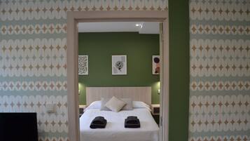 Habitación de hotel con cama, almohadas, una mesita de noche y un papel tapiz estampado.