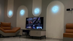 Habitación moderna con televisor de pantalla plana, dos sillones de cuero, un mueble bajo y luces decorativas con forma de luna en el techo.