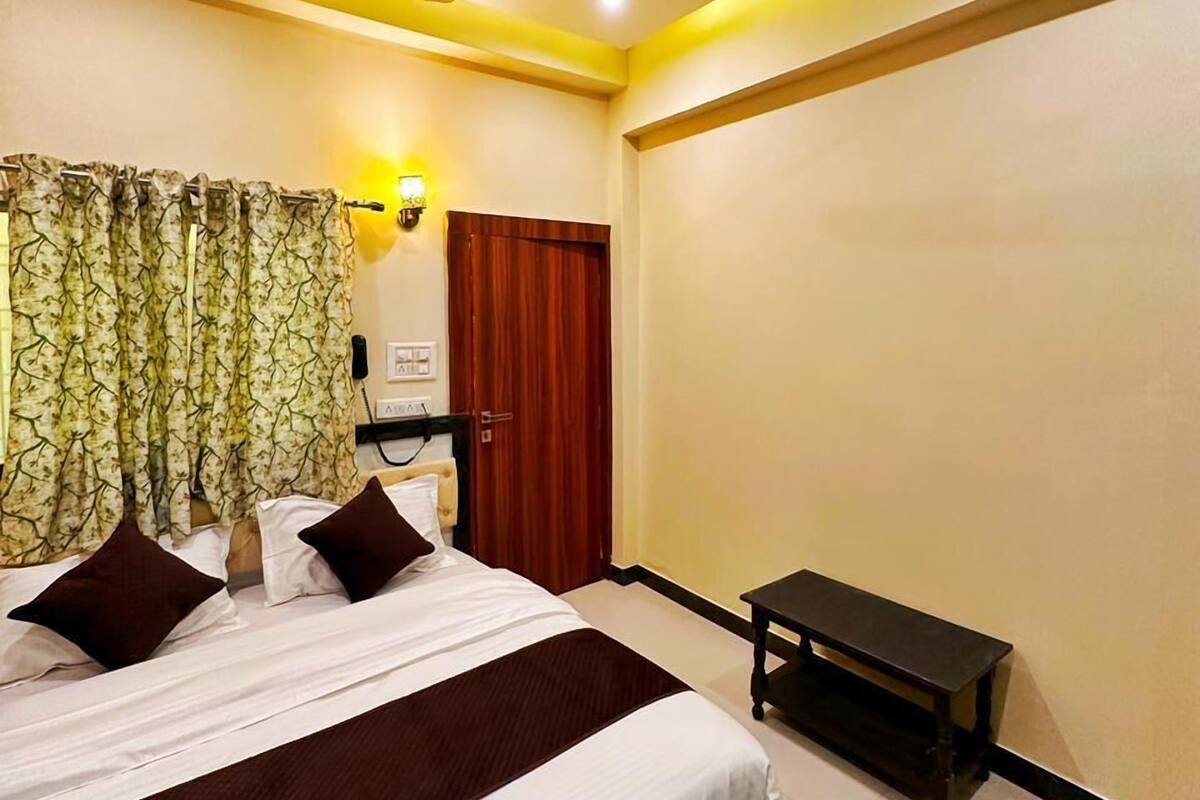 Quarto de hotel com cama, ventoinha no teto, mesa de cabeceira e janela com cortinas.