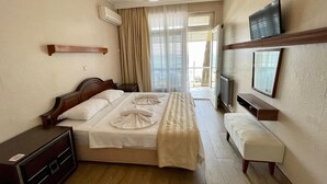 A hotel room with a bed, bedside table, TV, and a view of the outside. - Gülplaj Hotel (Erdek)