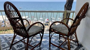 Two wicker chairs with cushions on a tiled balcony overlooking a beach with umbrellas and people. - Gülplaj Hotel (Erdek)