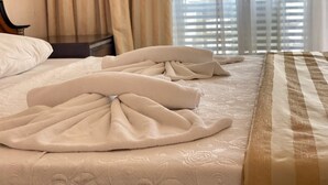 A hotel room with a neatly made bed, a nightstand, and a window with blinds. - Gülplaj Hotel (Erdek)