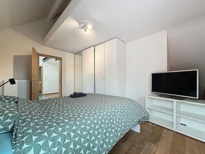 Een slaapkamer met een bed, een televisie op een meubelstuk, een kast en een spiegel.