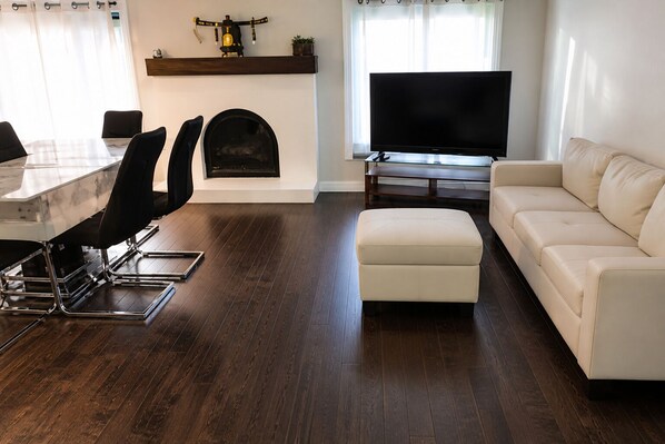 A living room with a sofa, ottoman, TV, fireplace, and dining area with chairs and a table.