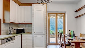 A kitchen with white cabinets, a microwave, and a dining area with a table and chairs. - Villa 'Porlezza Lake View' with Lake View, Air Conditioning, Private Pool, Ultra-Fast Wi-Fi (Cima)