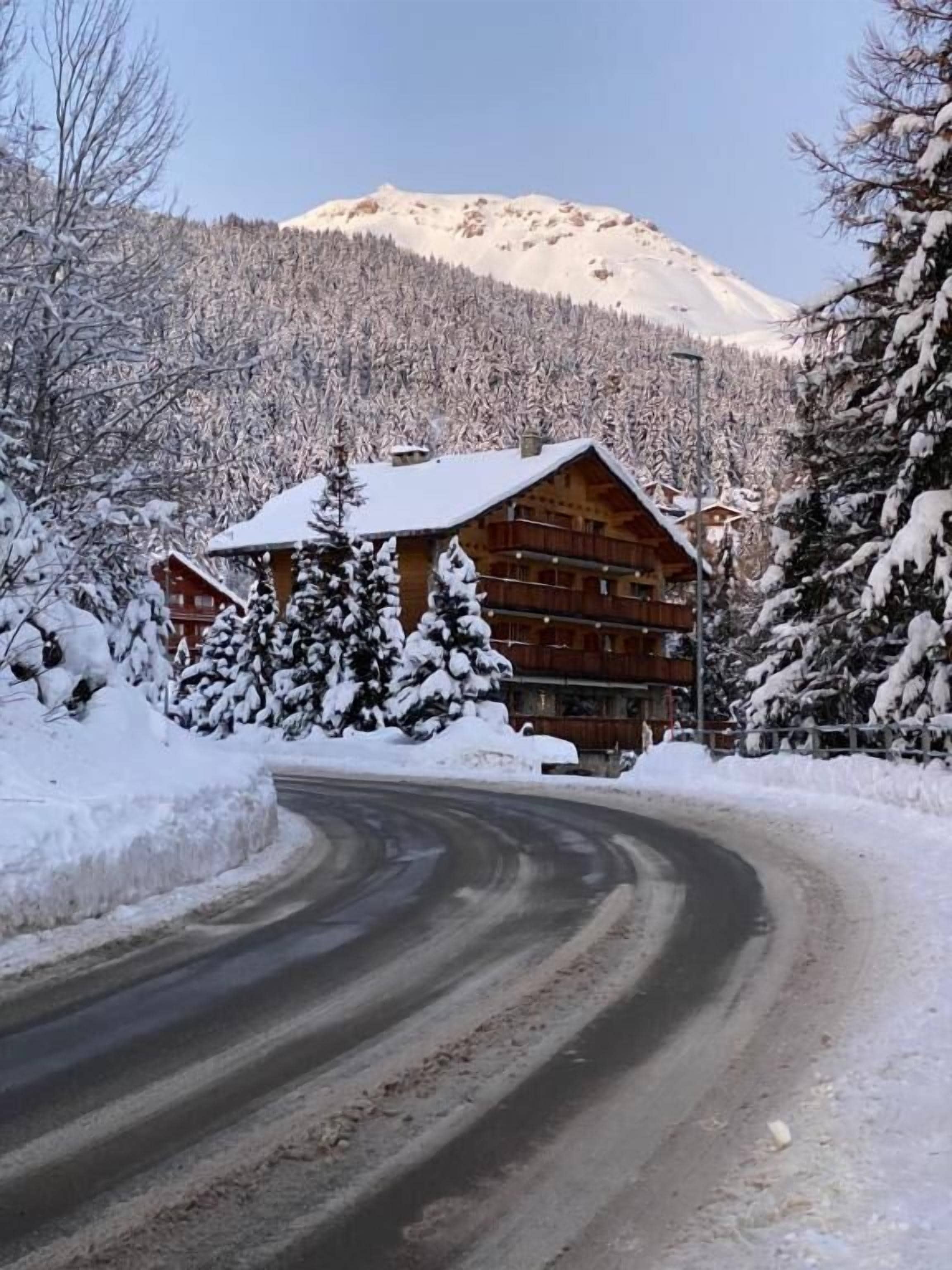 Eine Holzlodge mit einer geschwungenen Auffahrt, umgeben von schneebedeckten Bäumen und einem Berg im Hintergrund.