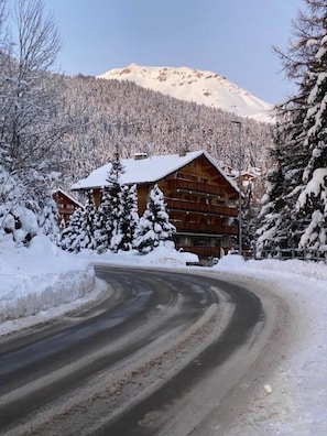 Eine Holzlodge mit einer geschwungenen Auffahrt, umgeben von schneebedeckten Bäumen und einem Berg im Hintergrund.