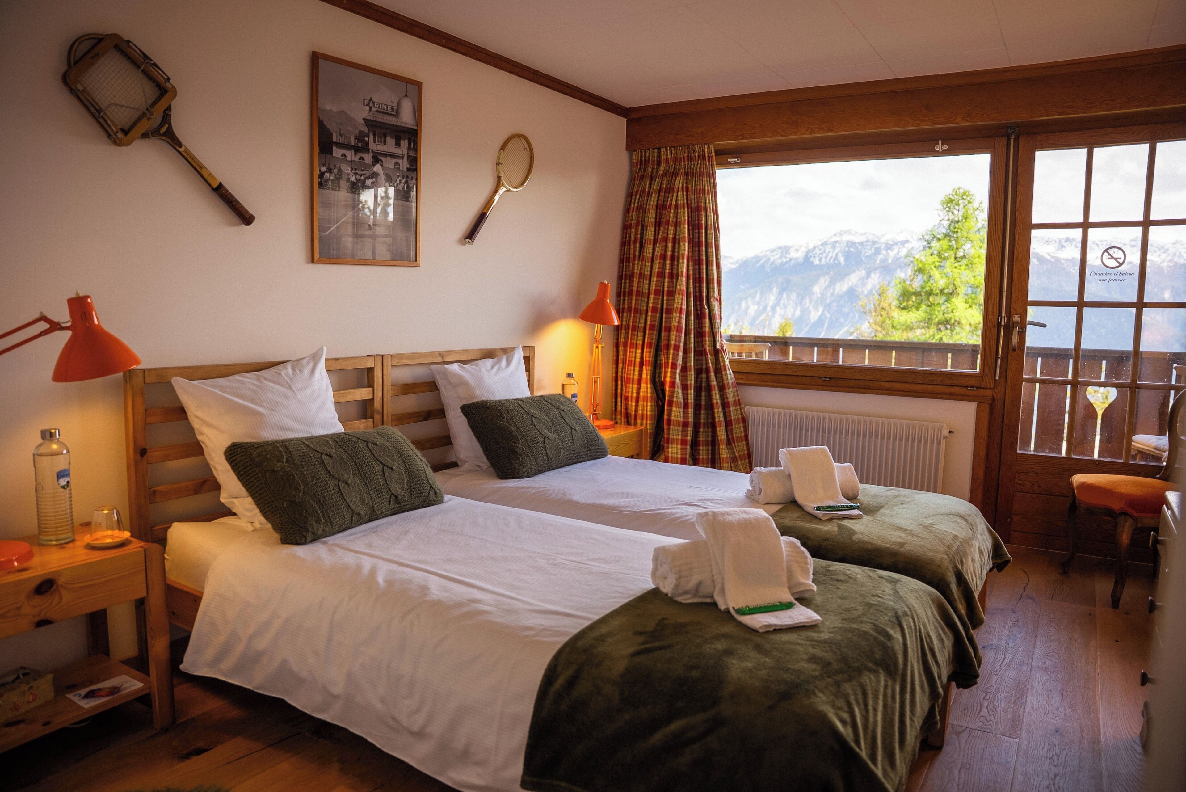 Habitación de hotel con dos camas, ventana con vistas a la montaña y una raqueta de tenis en la pared.