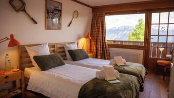 Habitación de hotel con dos camas, ventana con vistas a la montaña y una raqueta de tenis en la pared.