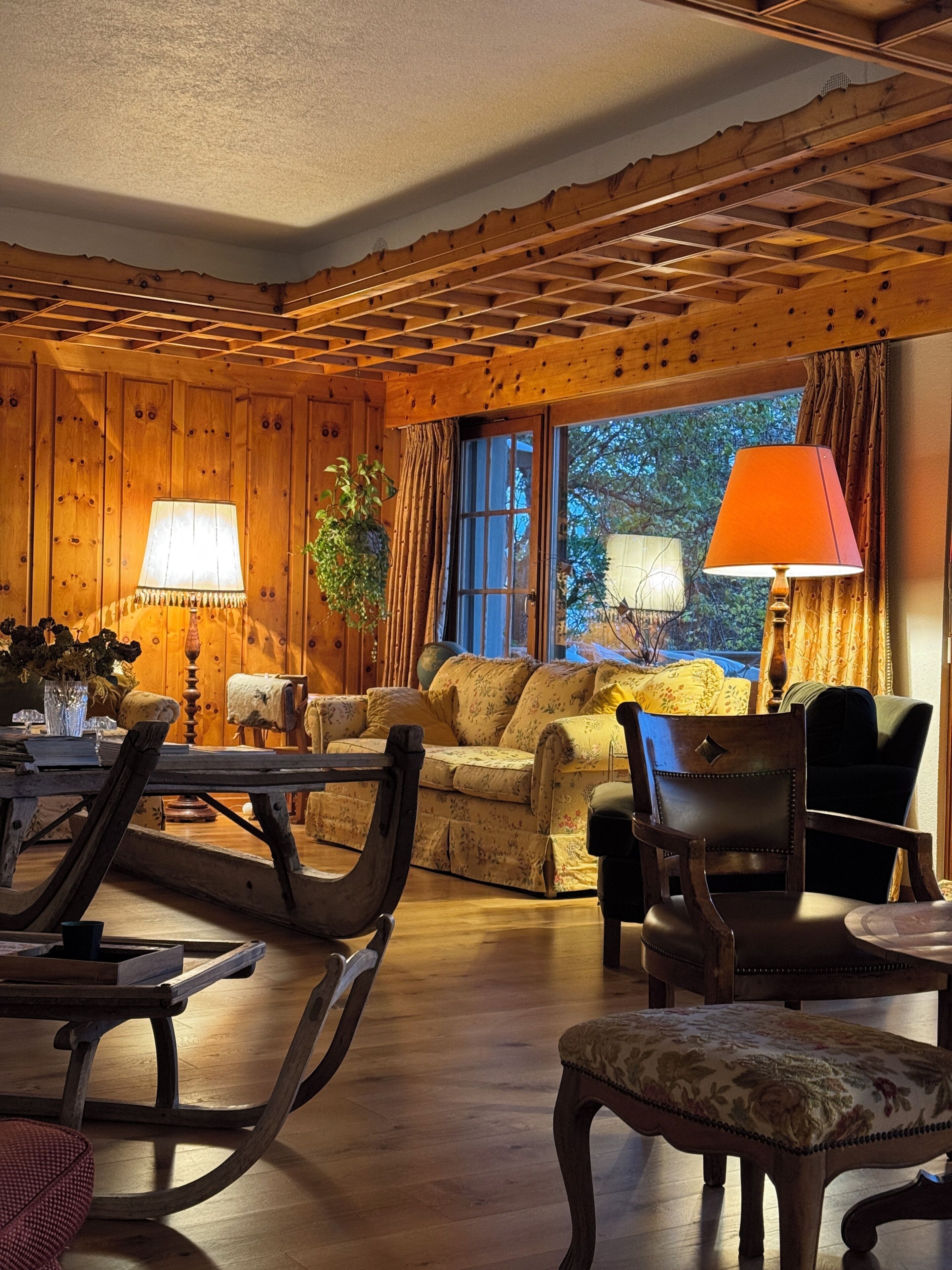 Ein gemütliches Zimmer mit Holzwänden, einer Couch, einem Esstisch mit Stühlen und einem Fenster mit Vorhängen.