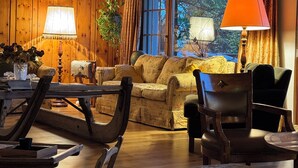 A cozy room with wooden walls, a sofa, a dining table with chairs, and a window with curtains.