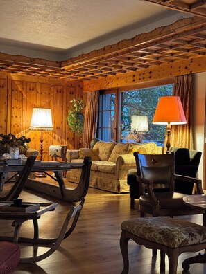 Ein gemütliches Zimmer mit Holzwänden, einer Couch, einem Esstisch mit Stühlen und einem Fenster mit Vorhängen.