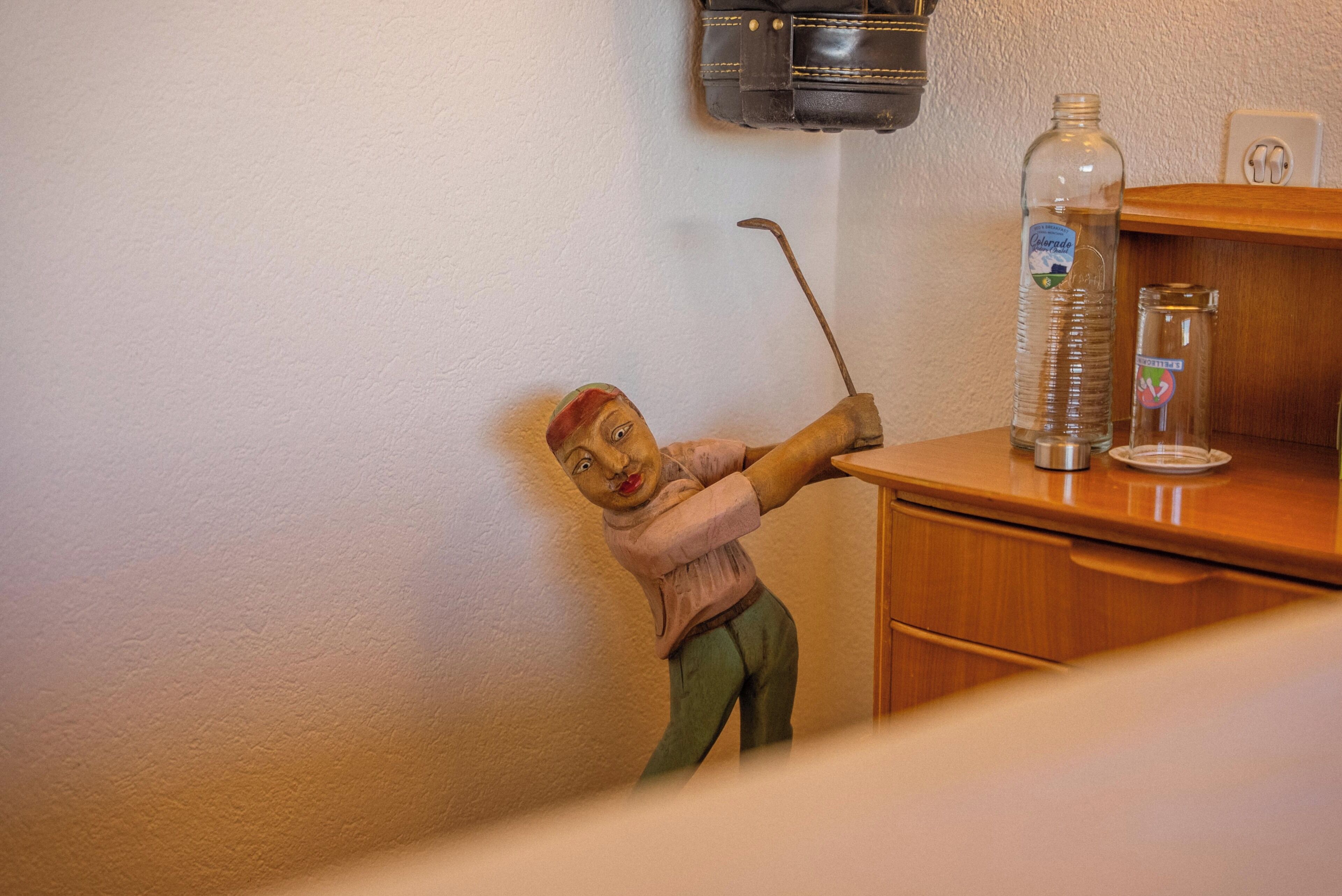 Eine Figur, die einen Golfschläger, eine Flasche und ein Glas auf einer Holztischplatte hält.