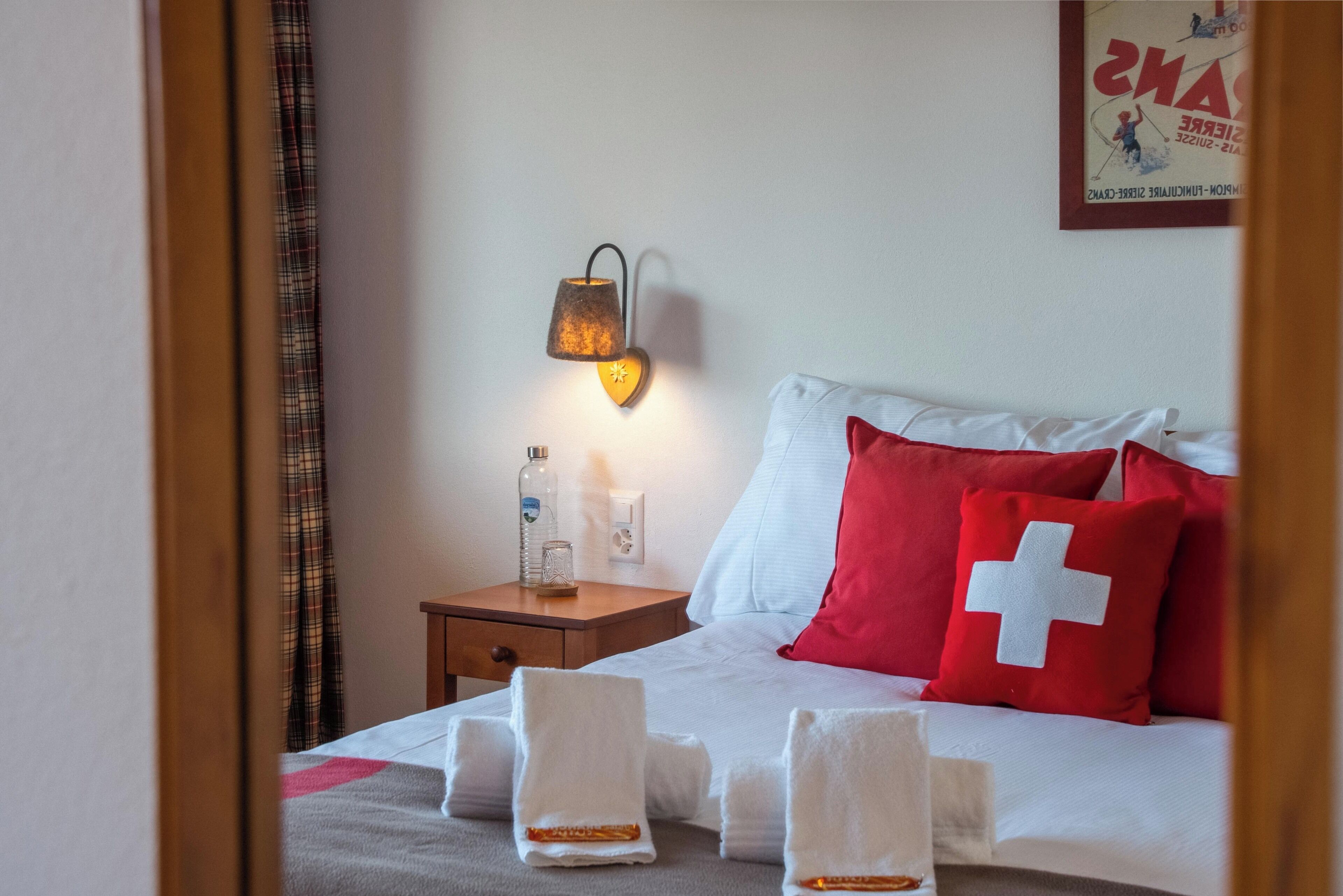 Habitación de hotel con cama, mesita de noche con lámpara, una botella y un vaso.