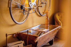 Una bicicleta colgada en la pared, un carro de madera con un florero y un sillón amarillo.