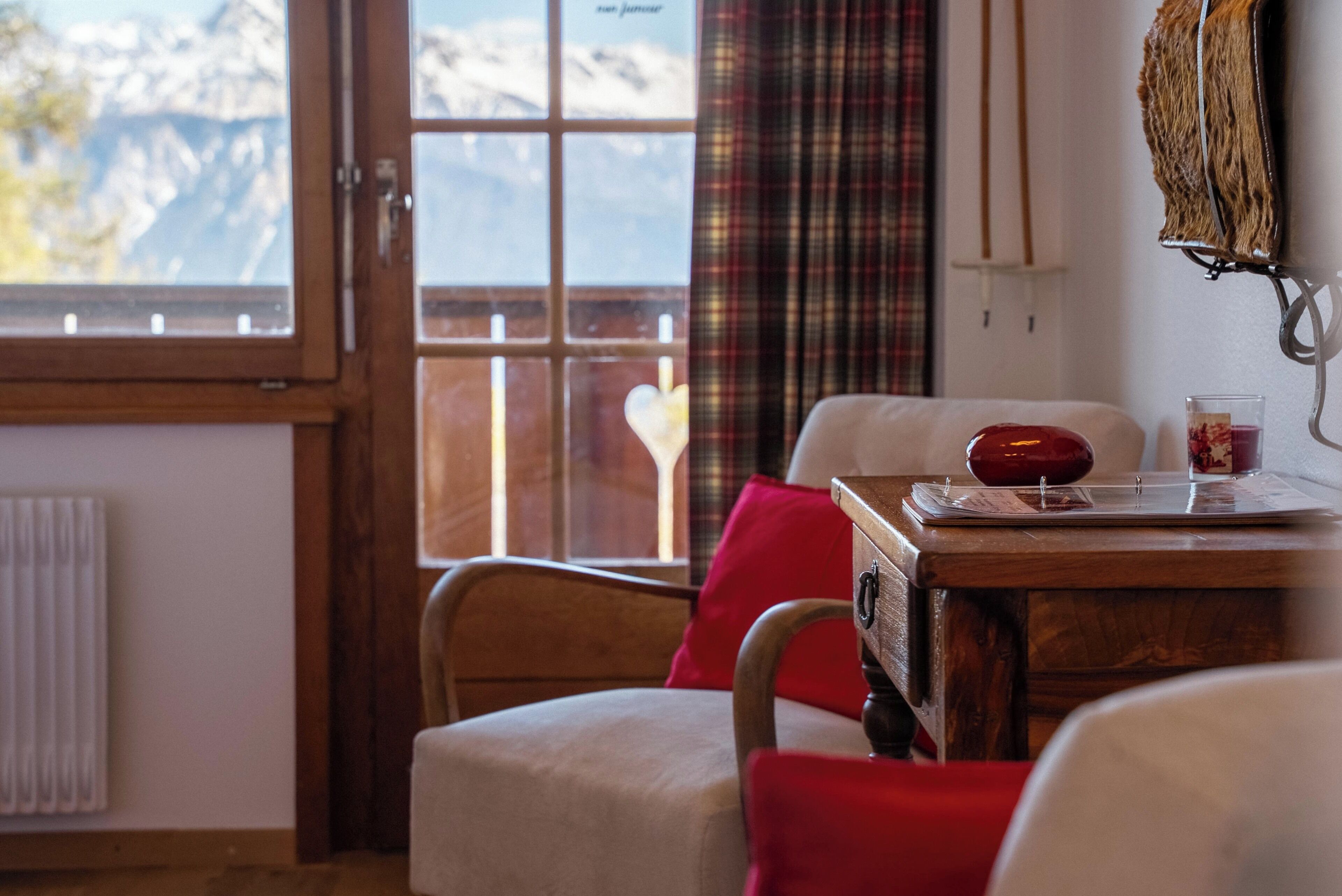 Ein gemütliches Zimmer mit Schreibtisch aus Holz, einem Sessel, einem Fenster mit Bergblick und einer Heizung.