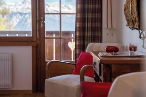Una habitación acogedora con un escritorio de madera, una silla, un ventanal con vistas a las montañas y un radiador.