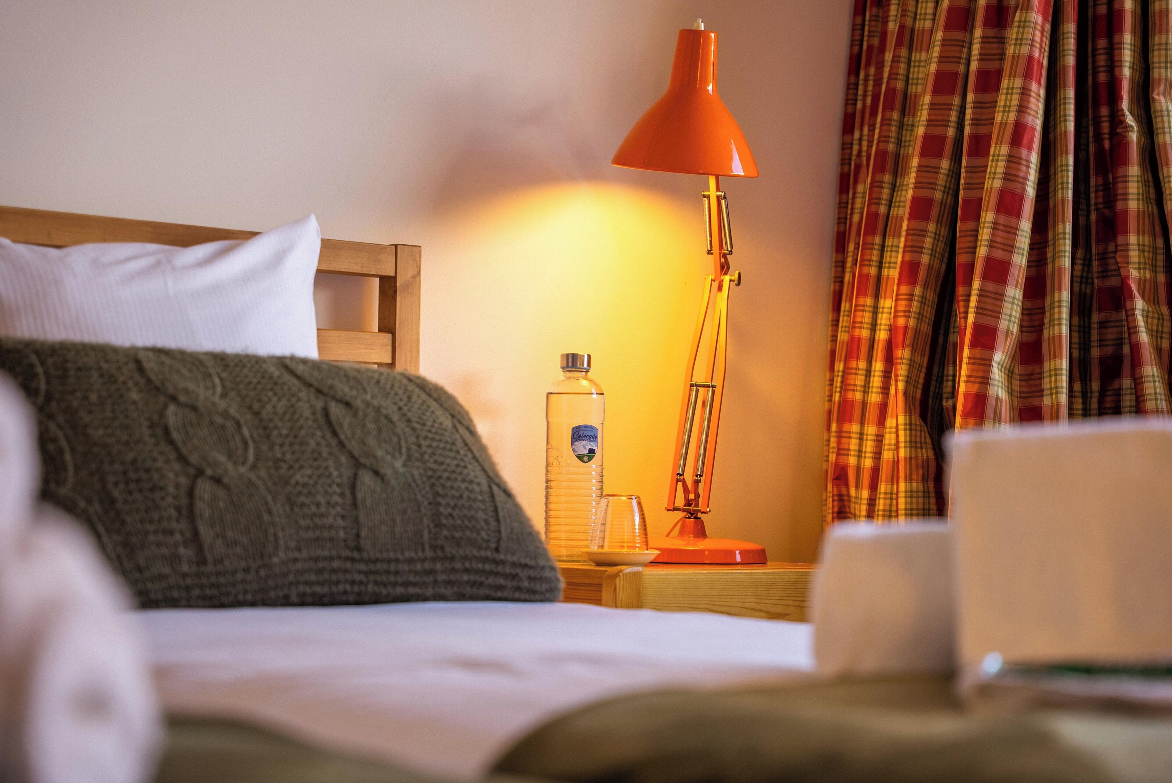 Una habitación de hotel con una cama, una mesita de noche, una lámpara, una botella y una taza.