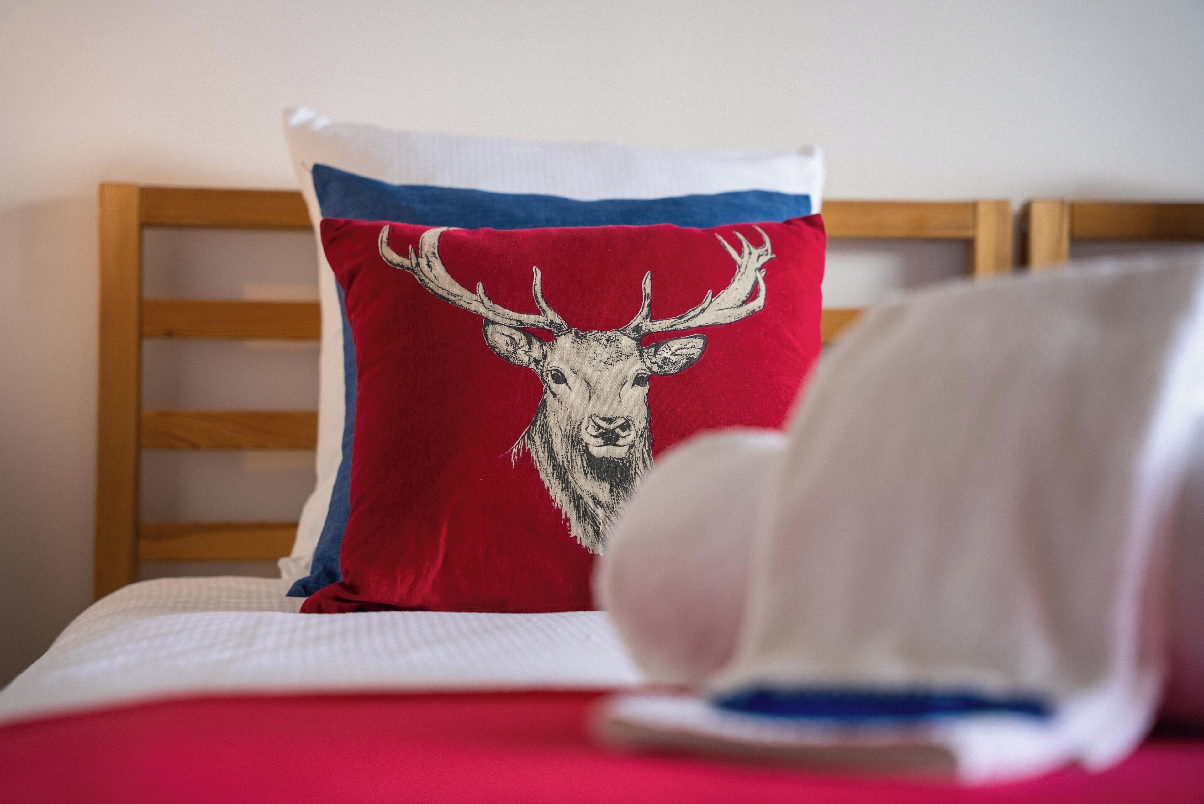 Una cama con un cojín rojo con diseño de cabeza de ciervo, un cojín blanco y un cabecero de madera.