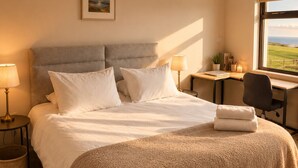 Quarto com cama, mesas de cabeceira, escrivaninha e janela com vista.