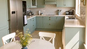 Uma cozinha com armários verde-água, geladeira de aço inoxidável, mesa de jantar branca com cadeiras e um vaso de flores.