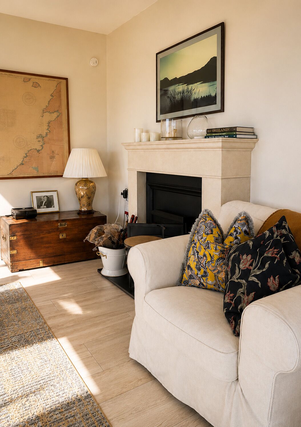 A living room with a fireplace, a sofa with patterned cushions, a map on the wall, and a lamp.