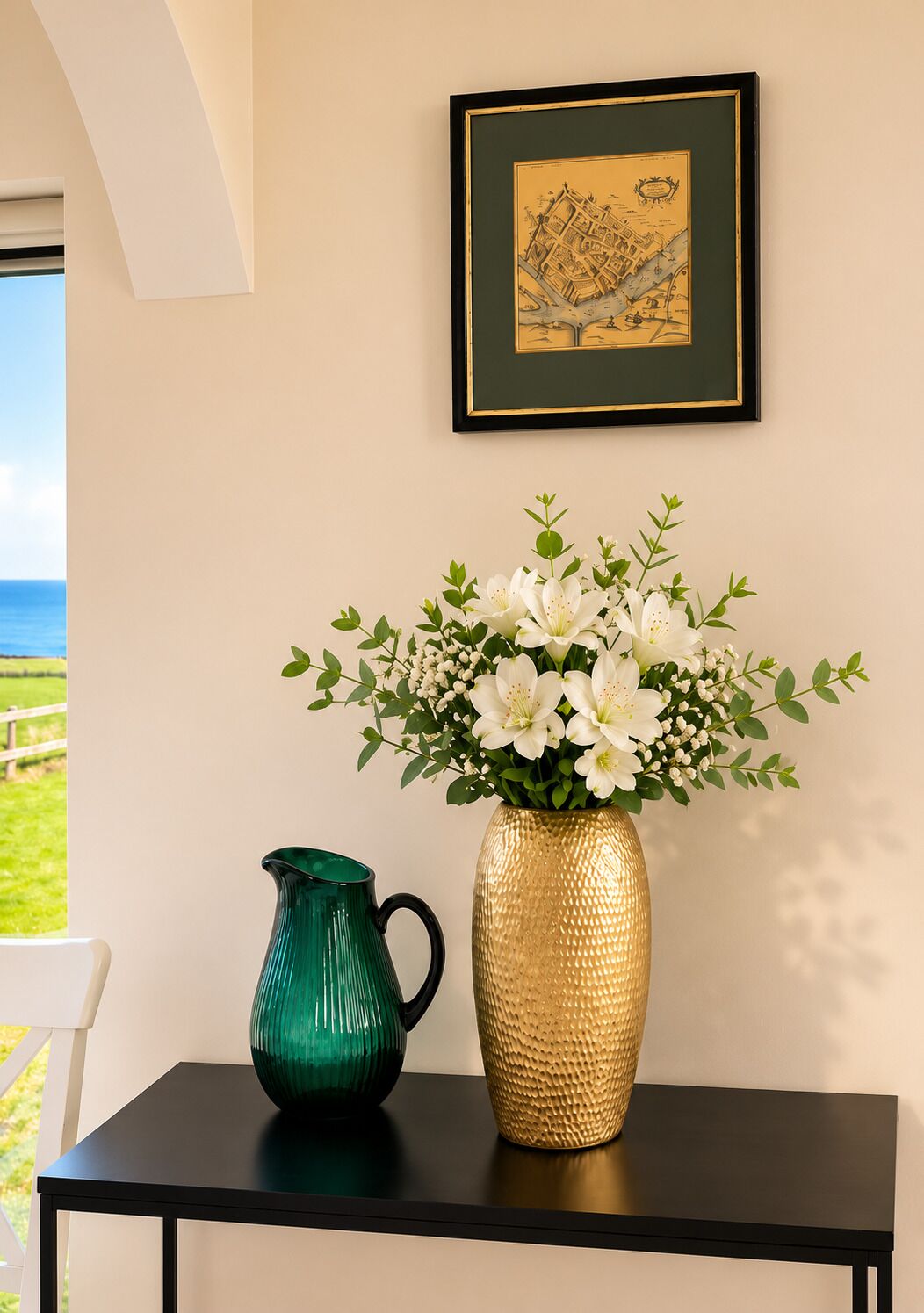 Una mesa con una jarra verde y un jarrón dorado con flores blancas.