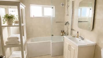 Ein modernes Badezimmer mit einer Badewanne, einer Toilette, einem Waschbecken und einer Dusche. Ein Regal mit Handtüchern und ein Blumentopf sind ebenfalls vorhanden.