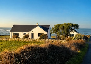 Ein Küstenhaus mit Steinmauer, einer grünen Vordergrundfläche und Blick auf das Meer.