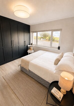 A bedroom with a large bed, a nightstand, a window, and dark wooden wardrobes.