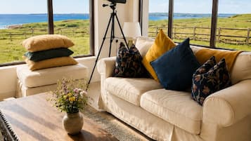 Un salón con vista al mar, un trípode y un sofá con cojines.