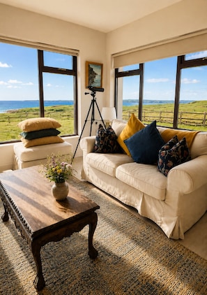 Sala de estar com vista para o mar, um tripé e um sofá com almofadas.