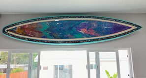 Ein Zimmer mit einem großen abstrakten Gemälde an der Wand, einer Schiebeglastür und Blick auf eine Wohngegend.