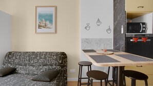 A modern living space with a sofa, a dining table with stools, a kitchen area, and a framed picture on the wall. - 'O'soleil' Apartment with Wi-Fi and Air Conditioning (Fréjus)