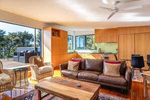 A spacious living area with a leather sofa, wooden coffee table, wicker chairs, and a view of the outdoors. - Hekerua Heights - premium holiday home with hot tub and ocean views, sleeps 6 (Waiheke Island)