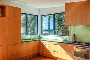 Een moderne keuken met houten kastjes, een groen aanrecht en een groot raam met uitzicht op bomen.