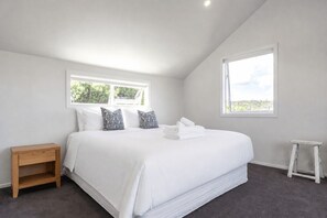 Ein Schlafzimmer mit einem großen Bett, zwei Fenstern, einem Nachttisch aus Holz und einem kleinen Hocker.