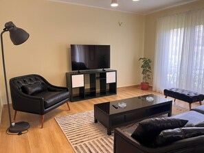 A modern living room with a flat-screen TV, leather armchair, ottoman, and a potted plant. - Spacious 3-bedroom apartment in the heart of Sheikh Zayed with Garden view (Giza Governorate)