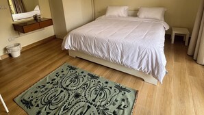 A hotel room with a bed, a bedside table, a mirror, a wardrobe, a hanging light fixture, and a patterned rug. - Spacious 3-bedroom apartment in the heart of Sheikh Zayed with Garden view (Giza Governorate)