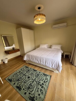 Hotelkamer met een bed, nachtkastje, spiegel, kledingkast, hanglamp en een kamerkleed met patroon.